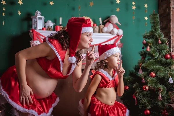 Christmas holiday. Pregnant woman and a little girl in a hat of Santa Claus. New Year — Stock Photo, Image