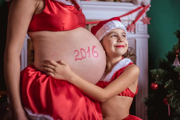 Pregnant woman and a little girl in a hat of Santa Claus. New Year — Stock Photo, Image