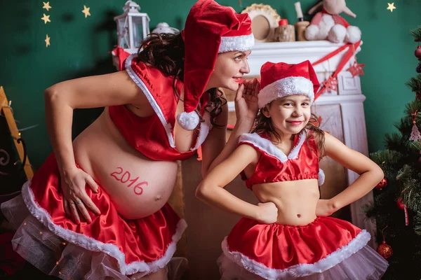 Christmas holiday. Pregnant woman and a little girl in a hat of Santa Claus. New Year — Stock Photo, Image