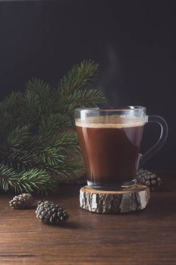 Bir fincan sıcak kahve ya da köknar dalları ve kozalaklarla süslenmiş koyu ahşap bir arka planda sıcak çikolata..