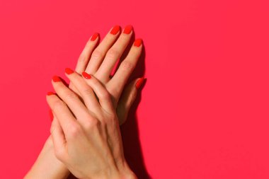 Kırmızı arka planda kırmızı ojeli manikürlü kadın tırnakları..