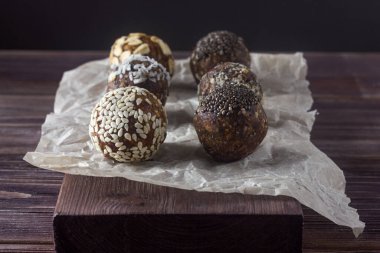 Raw vegan healthy energy balls with oatmeal, chia seed, coconut flakes, cocoa, almond and dried fruits on baking paper, dark wooden background. Close up.
