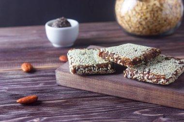 Raw vegan healthy energy bars or candy bars with oatmeal, cereals, nuts, seeds and dried fruits on dark wooden background. No cook energy bites.