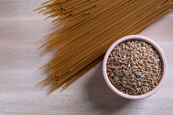 Spagetti ve kase, ahşap masada pişmemiş spelta taneleri. Üst görünüm.