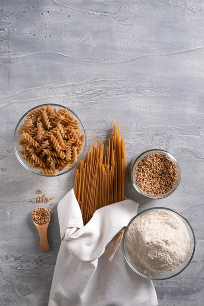 Spelt pasta, spelt grain and whole grain spelt flour in bowl and jar. Top view.