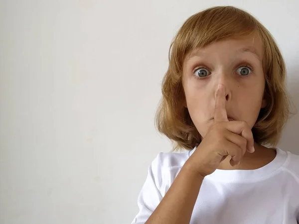 沈黙のジェスチャー 指は口の近くにある 白い背景の少女は沈黙を保つことのジェスチャーを示しています 金髪の7歳の子供 白人系 コピースペース テキストの場所 — ストック写真