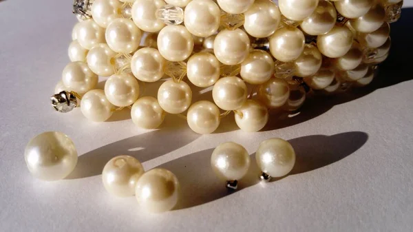 Gioielli di perle su sfondo bianco. Bracciale fatto a mano con perline sparse. Belle perline di delicato colore champagne. Decorazione femminile. — Foto Stock