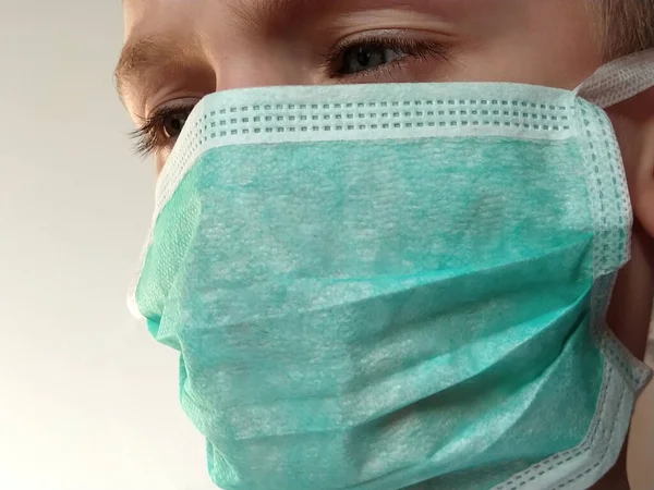 Masked child. The face of a 7-year-old boy in a protective surgical mask close-up. Schoolboy with blond hair and blue-gray eyes on white background.
