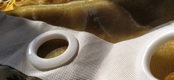 Plastic rings for attaching the fabric to the curtain rod. White plastic organza tulle eyelets. Light curtain in beige, brown or orange colors. White non-woven fabric. Finished textile edge. Interior element