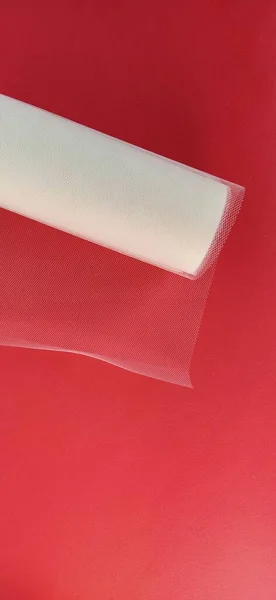 Fabric - white mesh in a roll on a red background. Nylon tape for tying bows on hair. A skein of tulle fabric. Copy space.