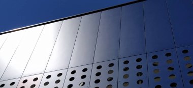 Modern bir binanın cephesi. Kırmızı, mavi ve beyaz levhalar ya da dekoratif delikli metal profiller. Dış yüzeyde teknolojik çözümler. Dekoratif elementler altında destekleyici yapılar inşa ediliyor.