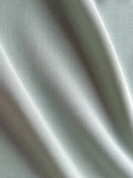 Beautifully folded light green fabric. Soft pleasant waves and flounces on textiles. Close-up. Drapery for curtains, fabric for dressmaking or upholstery.