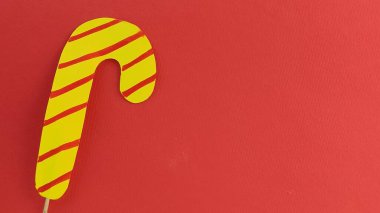 Kırmızı arka planda kağıttan yapılmış kıvrımlı sarı çizgili lolipop. Banner, boşluğu kopyala. Yeni yıl ya da Noel için kartpostal. Metin için boş alan. Şekerler, şekerler ve dekorasyonlar.