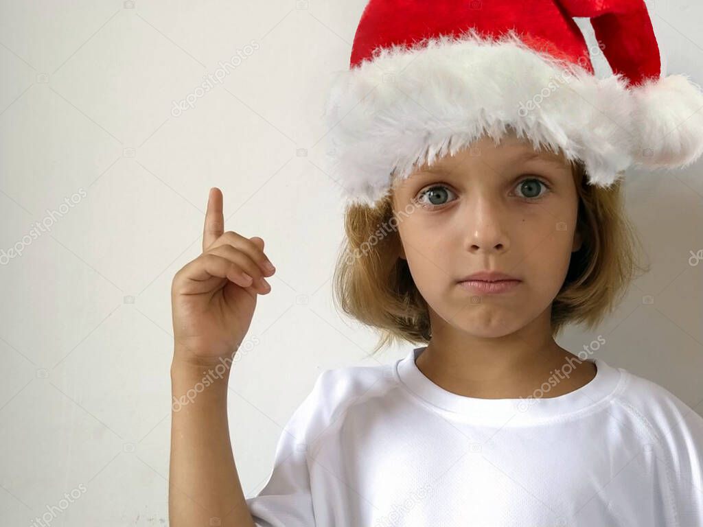 girl in santa claus hat. A child in a red hat with a white edging holds up hand and points something with his finger. Free space for text. New Year and Christmas theme for advertising and billboard.