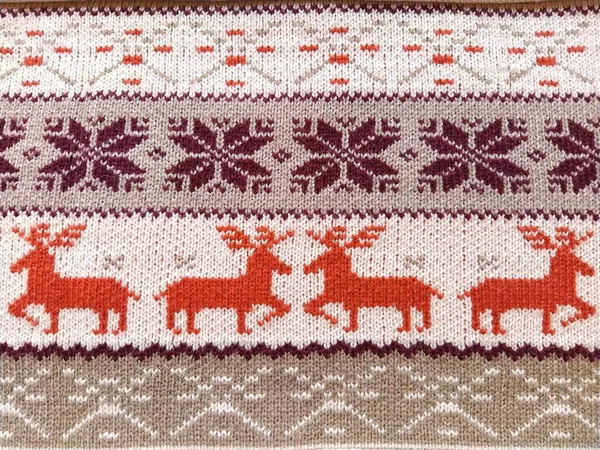 Knitted patterns with snowflakes, deer, flowers, broken stripes. Orange, red brown, white, beige woolen threads. Folk art. Warm winter sweater knitted with front loops. New Year\'s and Christmas.