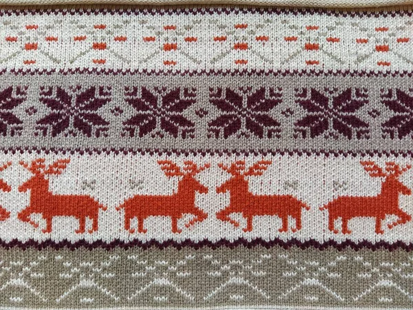 Knitted patterns with snowflakes, deer, flowers, broken stripes. Orange, red brown, white, beige woolen threads. Folk art. Warm winter sweater knitted with front loops. New Year\'s and Christmas.