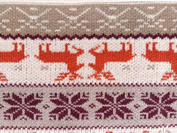Knitted patterns with snowflakes, deer, flowers, broken stripes. Orange, red brown, white, beige woolen threads. Folk art. Warm winter sweater knitted with front loops. New Years and Christmas