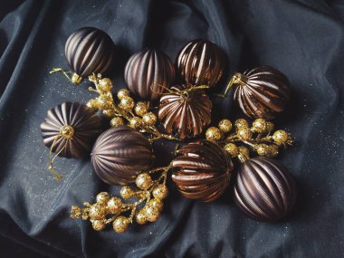 Yeni yıl için kart ve süslemeli noel kartı, Noel süslemeleri ve siyah arka planda parıltılar. Kahverengi çizgili toplar, çiçekler ve beyaz kar taneleri, böğürtlenli altın dallar.