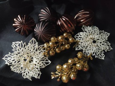 Yeni yıl için kart ve süslemeli noel kartı, Noel süslemeleri ve siyah arka planda parıltılar. Kahverengi çizgili toplar, çiçekler ve beyaz kar taneleri, böğürtlenli altın dallar.