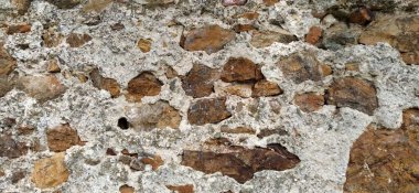 Taş duvar. Sıcak renklerde büyük tuğlalar ve kaldırım taşları yığılmış. Duvarın yüzeyinden çıkan gevşek beyaz taşlar.