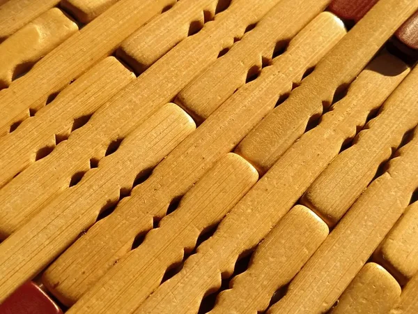 reed or wood mat. The rug is a mat under the hot. Knitted processed wood sticks with rounded edges. Close-up. Yellow, brown and beige colors. Side lighting. Traditional bamboo pad texture.