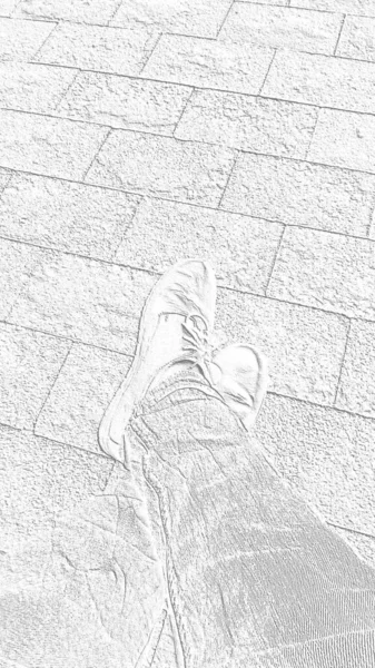 Feet in boots against the background of street tiles or the road. Two seated legs crossed, photographed from above while sitting. Monochrome white and gray image. Vertical image — Stock Photo, Image