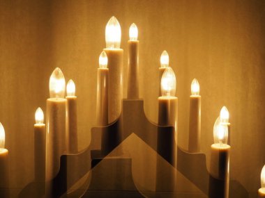 Schwibbogen kemeri, bir şamdan şeklinde parlıyor. Sarı arka plan. Akşam, romantik, şenlikli, dini ya da mistik atmosfer. Mum ışığını andıran yanan ampuller. Çift pozlama.