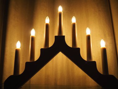 Schwibbogen kemeri, üçgen bir şamdan şeklinde. Sarı arka plan. Akşam, romantik, şenlikli, dini ya da mistik atmosfer. Mum ışığına benzeyen yanan ampuller.