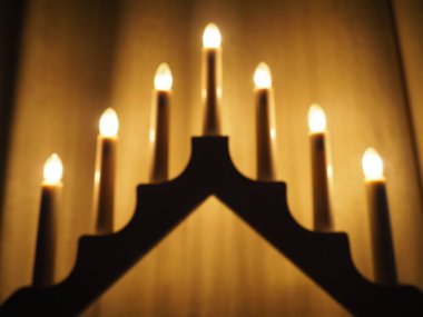 Schwibbogen kemeri, üçgen bir şamdan şeklinde. Sarı arka plan. Akşam, romantik, şenlikli, dini ya da mistik atmosfer. Mum ışığına benzeyen yanan ampuller.