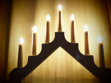 Schwibbogen kemeri, üçgen bir şamdan şeklinde. Sarı arka plan. Romantik, şenlikli, dini ya da mistik bir atmosfer. Mum ışığına benzeyen yanan ampuller, yumuşak odak.