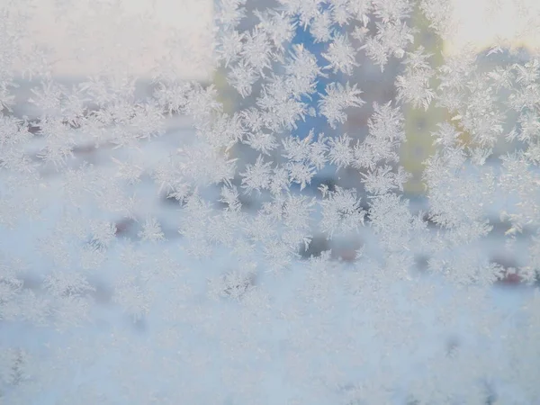 窗上的冰图案 漂亮的卷发和玻璃上的水晶 窗外有蓝色的冬日的天空 雪和一条城市街道 新年及圣诞动机 — 图库照片