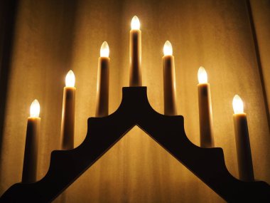 Schwibbogen kemeri, üçgen bir şamdan şeklinde. Sarı arka plan. Akşam, romantik, şenlikli, dini ya da mistik atmosfer. Mum ışığına benzeyen yanan ampuller.