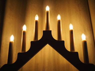 Schwibbogen kemeri, üçgen bir şamdan şeklinde. Sarı arka plan. Akşam, romantik, şenlikli, dini ya da mistik atmosfer. Mum ışığına benzeyen yanan ampuller.