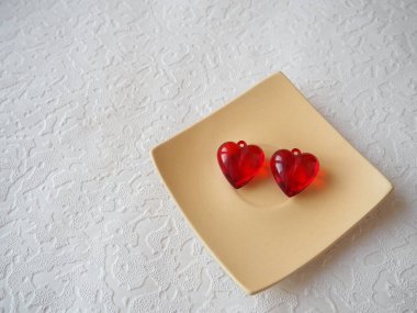 Sevgililer Günü. Beyaz bir plakada kırmızı şeffaf plastik küpeler ve beyaz. Sevgililer günü için beyaz arkaplanlı tebrik kartı. Aşkın ifadesi. Boşluğu kopyala.