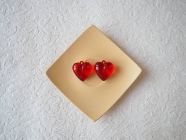 Sevgililer Günü. Beyaz bir plakada kırmızı şeffaf plastik küpeler ve beyaz. Sevgililer günü için beyaz arkaplanlı tebrik kartı. Aşkın ifadesi. Boşluğu kopyala.