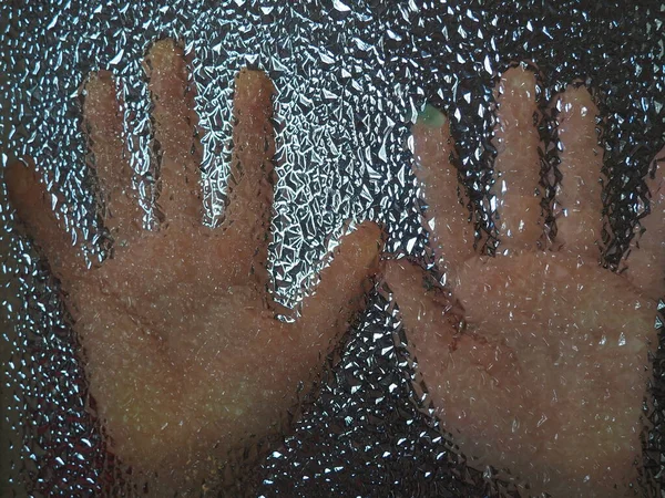 Horror hands. The shadow hands of human behind the glass. Corrugated textured glass through which children's palms are visible