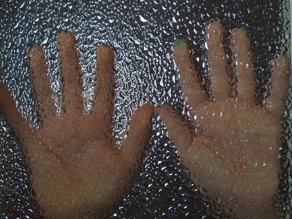 Horror hands. The shadow hands of human behind the glass. Corrugated textured glass through which children\'s palms are visible