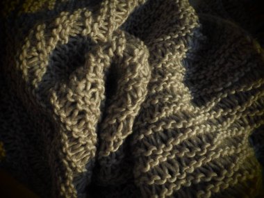 Büyük kahverengi ya da gri iplikten örülmüş eşarp. Gür makine örgü örüyor. Sonbahar-kış dönemi için sıcak bir gardırop seçeneği. Öne dokuma, mor düğümler. Samimi ev hala hayat.