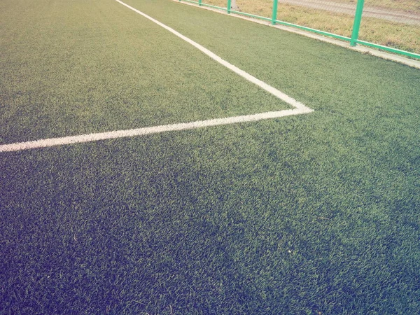 The marking of the football field on the green grass. White lines no more than 12 cm or 5 inches wide. Football field area. Side lines, goal lines. Sun glare. Color and light gradient.