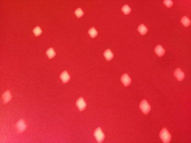 Puantiyeli kırmızı arka plan. Güneşin ışınları jaluzilerdeki deliklerden parlıyor ve renkli yüzeydeki ışık bulanık daireler çiziyor..