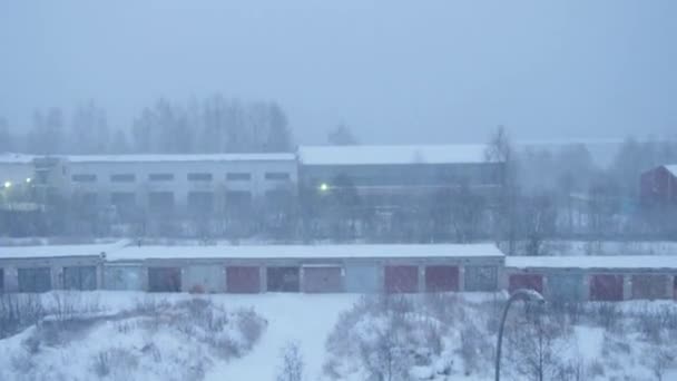 城市郊区下着暴风雪和大雪。由于冬季气候条件，能见度低。非飞行的天气。工厂的建筑物被雪覆盖着.风暴中的城市景观 — 图库视频影像