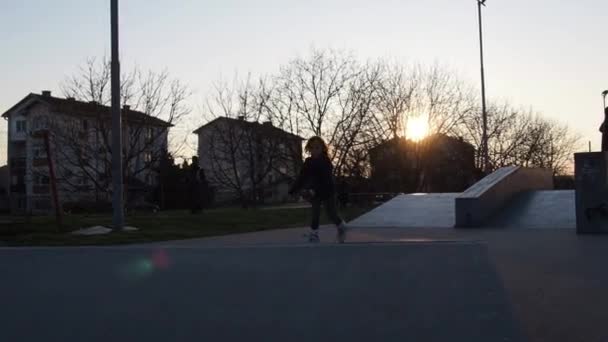 En 7-årig flicka rullar rollerblading på idrottsplatsen. Barnet rullar på en bula på rullar och rullar ner på andra sidan. Aktivitet eller träning utomhus. Flicka med blont långt hår och grå ögon — Stockvideo