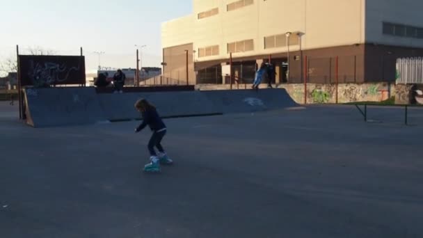 Een jongen en een meisje zijn aan het rolschaatsen, rijdend op een heuvel - een obstakel. Vrije tijd. Sporttraining op het terrein. 7 maart 2021 Sremska Mitrovica, Servië. Mensen en fietsers op de achtergrond — Stockvideo