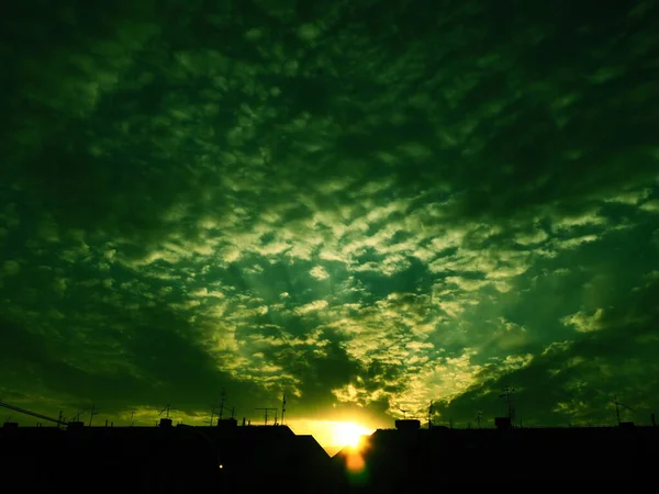 Sunset over the city rooftops. Clouds in the evening sky. The sun\'s rays pierce the clouds. Green - yellow colors of the sky and clouds. Beautiful landscape. The sun goes down.