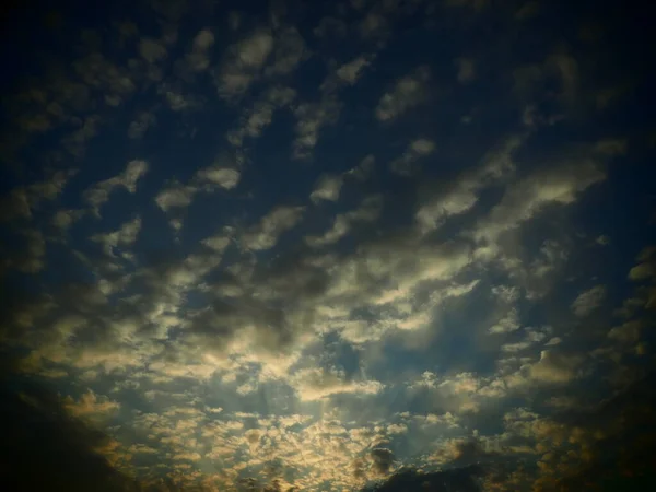 Clouds in the evening sky. The sun's rays pierce the clouds. Blue, yellow and orange colors of the sky and clouds. Beautiful landscape. The sun goes down.