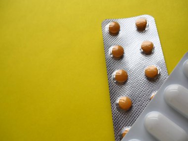 Sarı arka planda bir sürü hap. Hastalıkların tedavisi için kapsüllü haplar, vitaminler ve kabarcıklar. Boşluğu kopyala