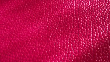 Yapay deri parlak pembe ya da fuşya renginde. Bir çanta ya da ayakkabının yüzeyindeki belirgin izler ve yükseklikler. Işığın yansıması. Taklit domuz derisinden yapılmış moda aksesuarı. Yakın plan.