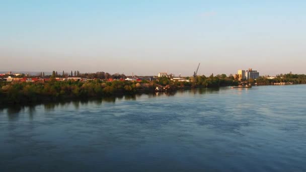 A folyó partja ipari területtel. Vízáramlás a Száva folyón, Szerbia, Sremska Mitrovica, Balkán. Hűtse le magát a víz felszínén. Arany óra. Épületek, gyárszerkezetek — Stock videók