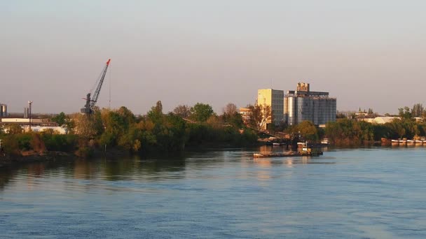 Az uszály egy ipari zónával indul a folyópartról. Vízáramlás a Száva folyón, Szerbia, Sremska Mitrovica. Hűtés a víz felszínén. — Stock videók