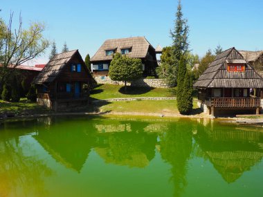 Stanisici, Bijelina, Bosna-Hersek. 25 Nisan 2021 Ethno köyü, Bosna tarzı dağlık bölgelerde kütüklerden yapılmış geleneksel köy evleri. Sulu göl. Ahşap mimari